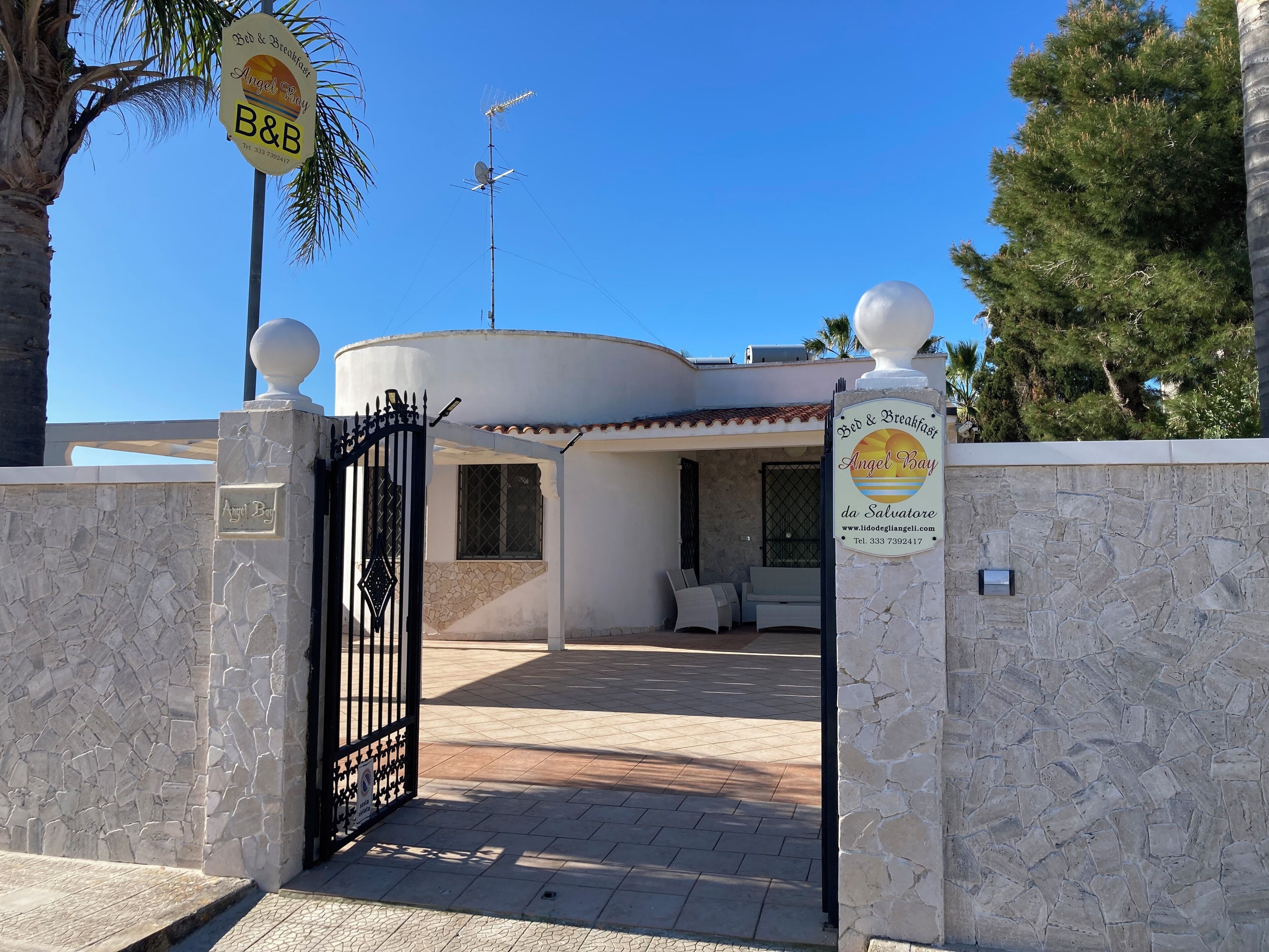 Une entrée fermée par un portail mène à la propriété appelée Angel Bay B&B, qui se caractérise par un mur en pierre, un portail et un ciel dégagé.