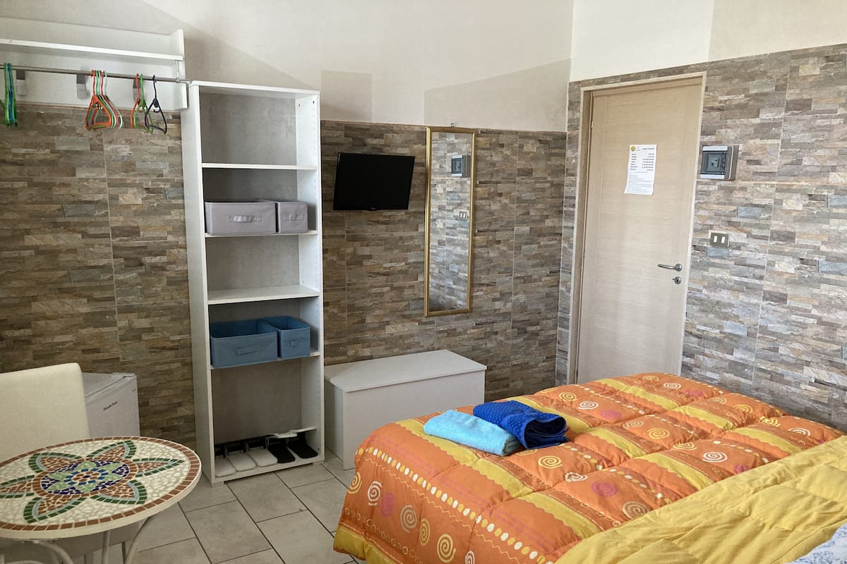 A hotel room with a bed, a desk, a chair, a small table, a wardrobe, and a TV.