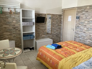 Habitación de hotel con cama, escritorio, silla, mesita, armario y televisor.