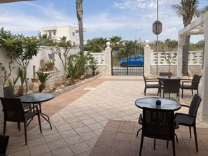 Un patio al aire libre con suelo de baldosas, muebles de mimbre negro y plantas en macetas.