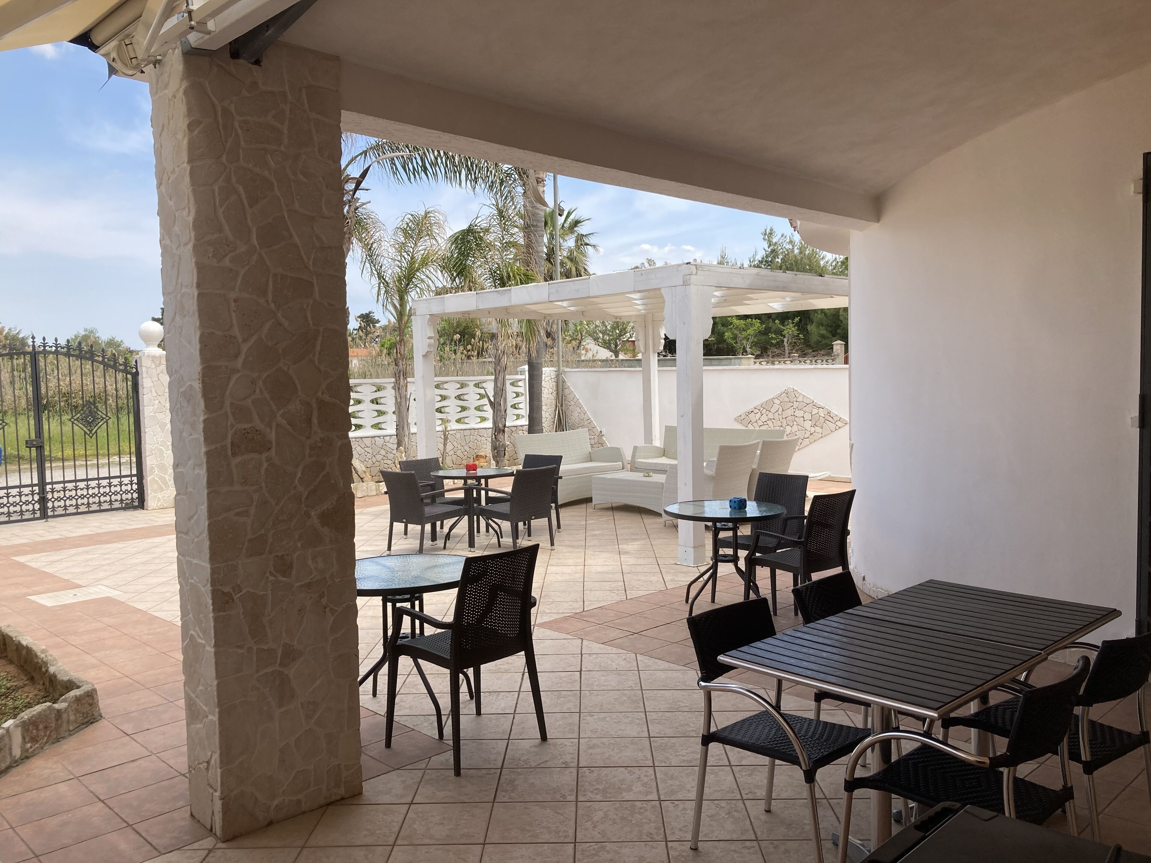 An outdoor patio area with stone pillars, a white pergola, and a seating arrangement including tables and chairs.