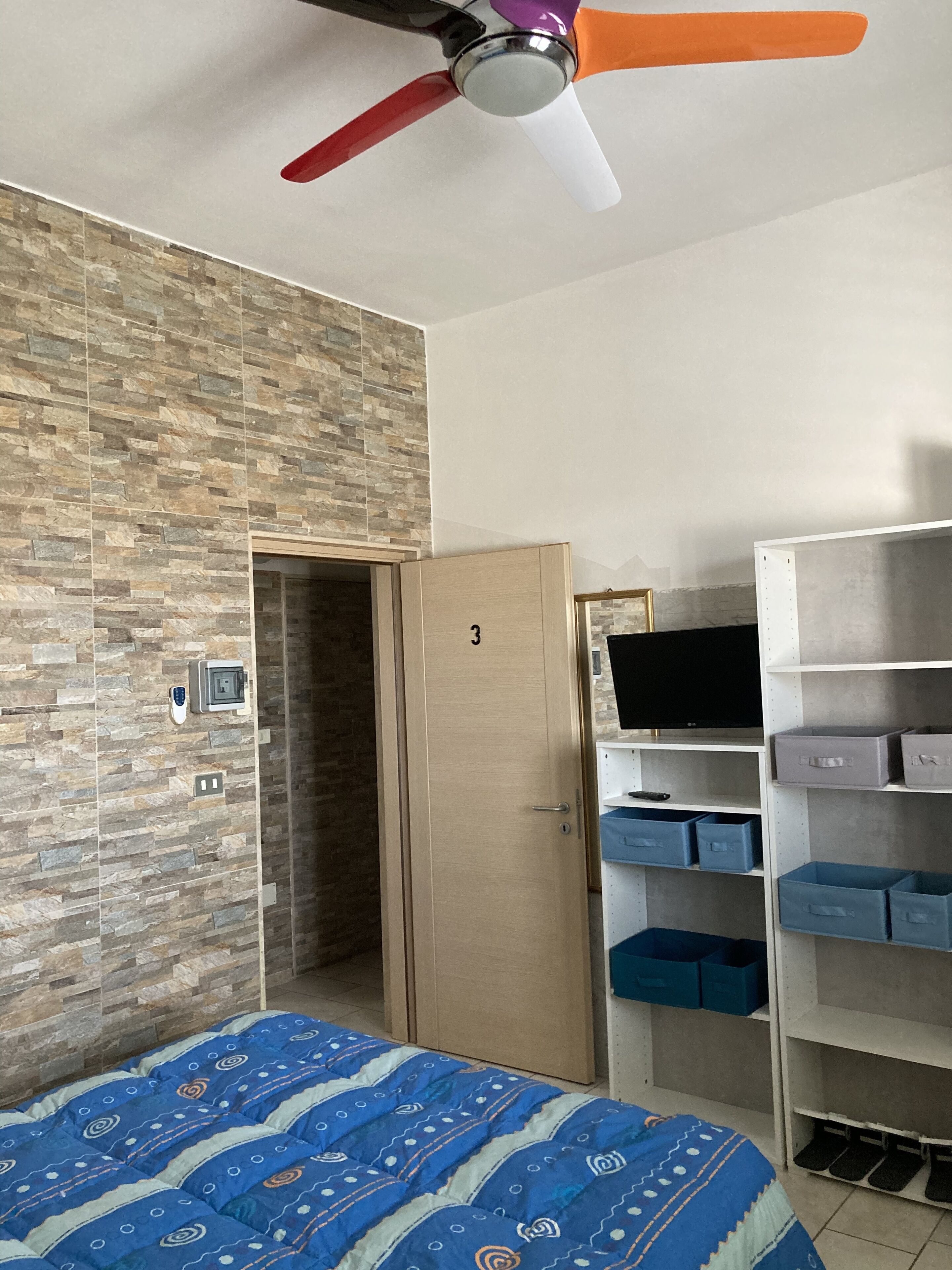 Ein Schlafzimmer mit Bett, Kleiderschrank, Fernseher und Deckenventilator.