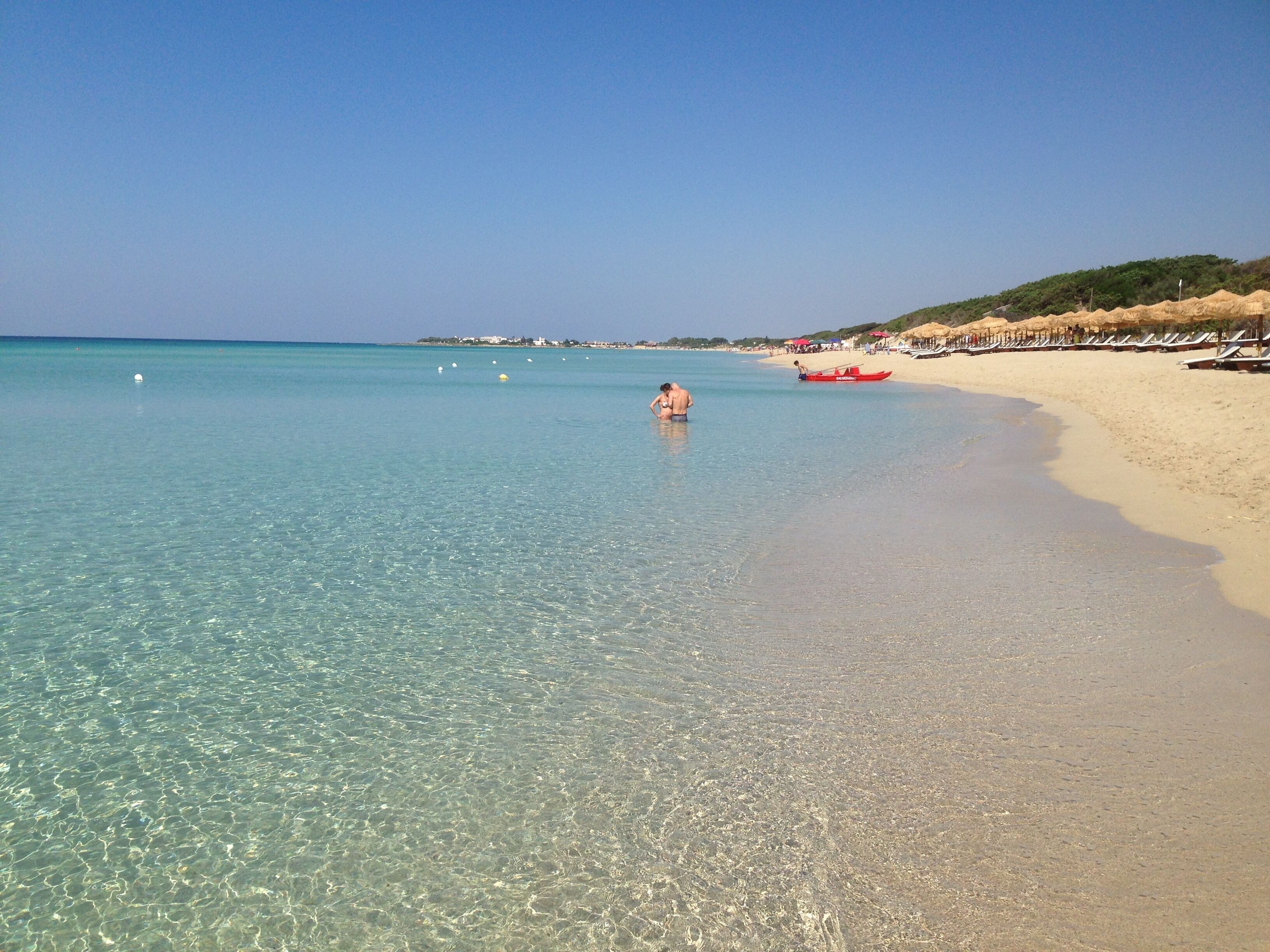 Una spiaggia con acque cristalline, una riva sabbiosa e una barca rossa.