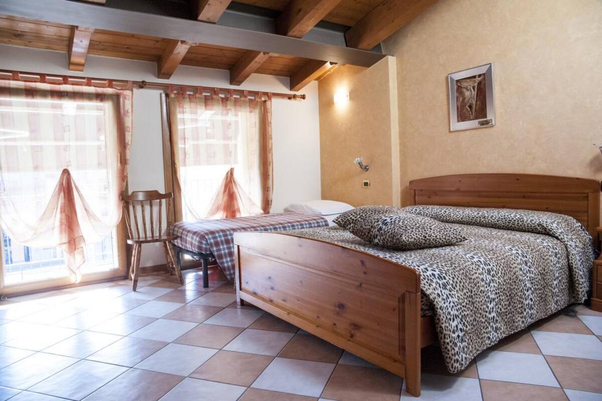 A bedroom with a wooden bed, a chair, and a window with curtains.