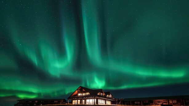 A house with a large balcony under a night sky with green aurora borealis. - Hotel Rangá (Rangárþing ytra)