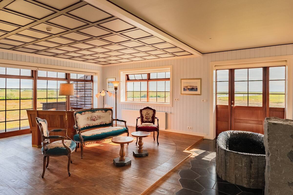 Quarto espaçoso com piso de madeira, lareira e grandes janelas com vista para o exterior.