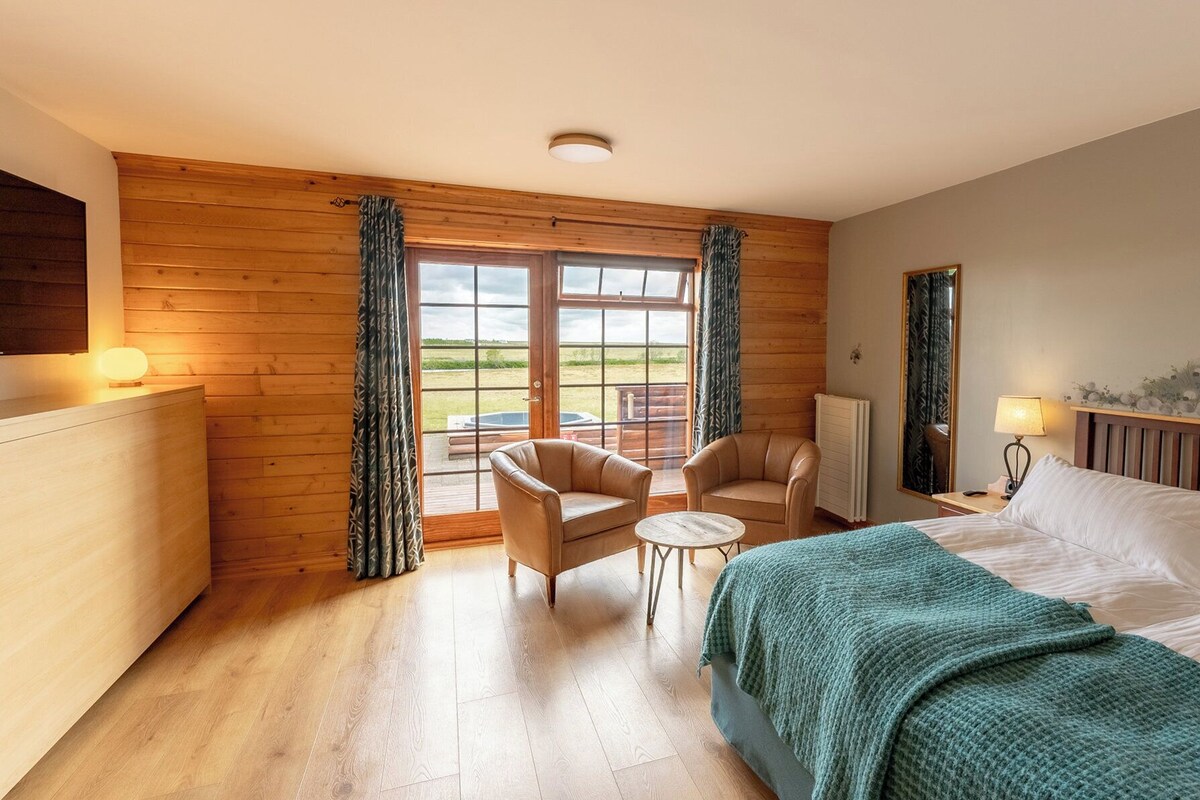 A bedroom with a bed, two chairs, a small table, and a view of the outdoors through a large window.