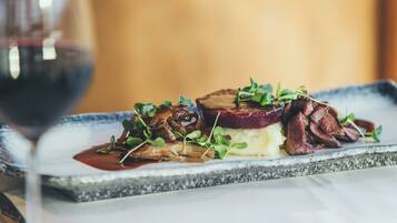 A plated dish with meat, mushrooms, and greens, accompanied by a glass of red wine.