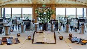 A restaurant with a high wooden ceiling, large windows, and tables set with menus, candles, and silver buckets. - Hotel Rangá (Rangárþing ytra)