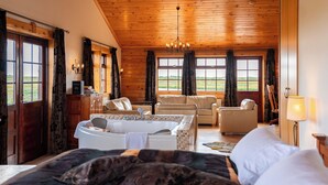 A cozy room with a large bed, a sofa, a chair, and a small table. There are windows with curtains, a chandelier, and a view of the outdoors. - Hotel Rangá (Rangárþing ytra)