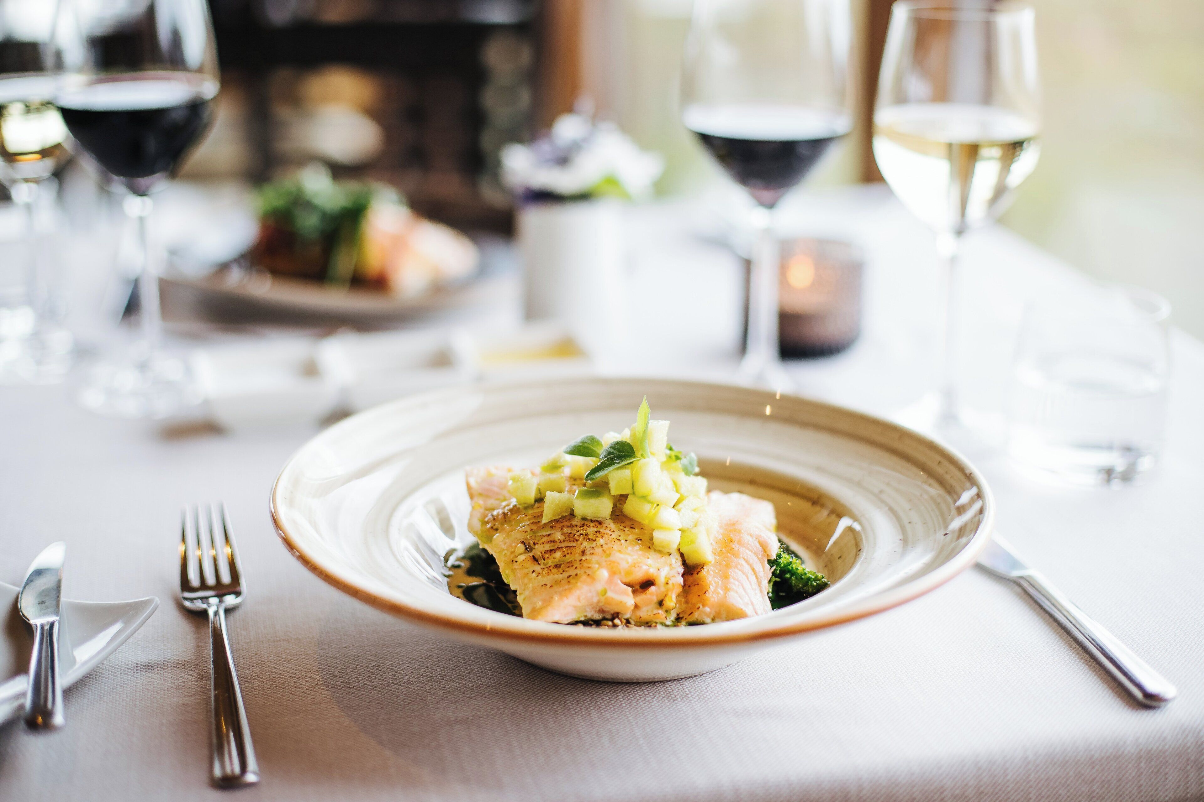 A dining table with a plate of food, cutlery, and glasses of wine.