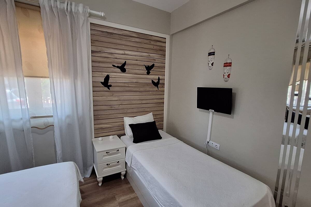 A bedroom with two beds, a wooden headboard, a TV mounted on the wall, and a window with curtains.