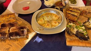 Una mesa de comedor con varios platos, incluyendo un bol de papas, alimentos a la parrilla y un plato con un elemento rojo.