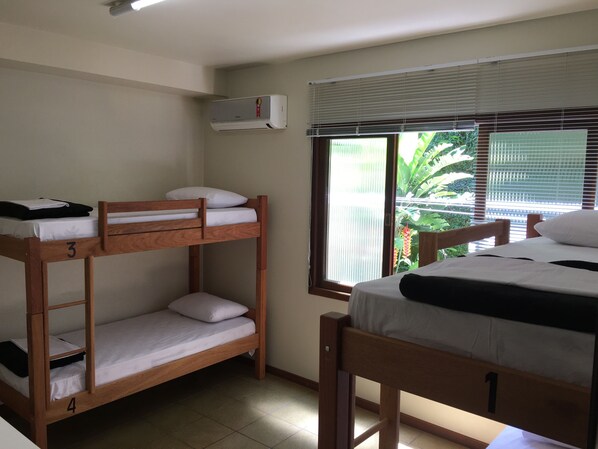 A dormitory room with bunk beds, a window with blinds, and an air conditioning unit.
