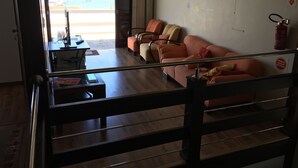 Una sala de estar con un sofá, una mesita de centro y un televisor. Se ve una playa y un paisaje urbano a través de un ventanal grande.