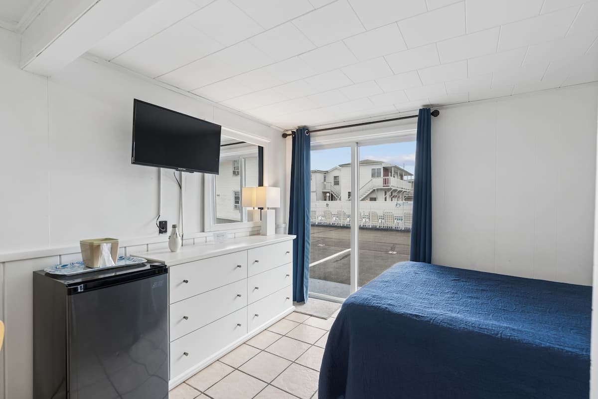 A hotel room with a bed, a TV mounted on the wall, a dresser, and a window with curtains.