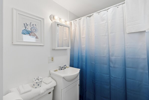 A bathroom with a white sink, a framed artwork, a mirror with lights, and a blue shower curtain.