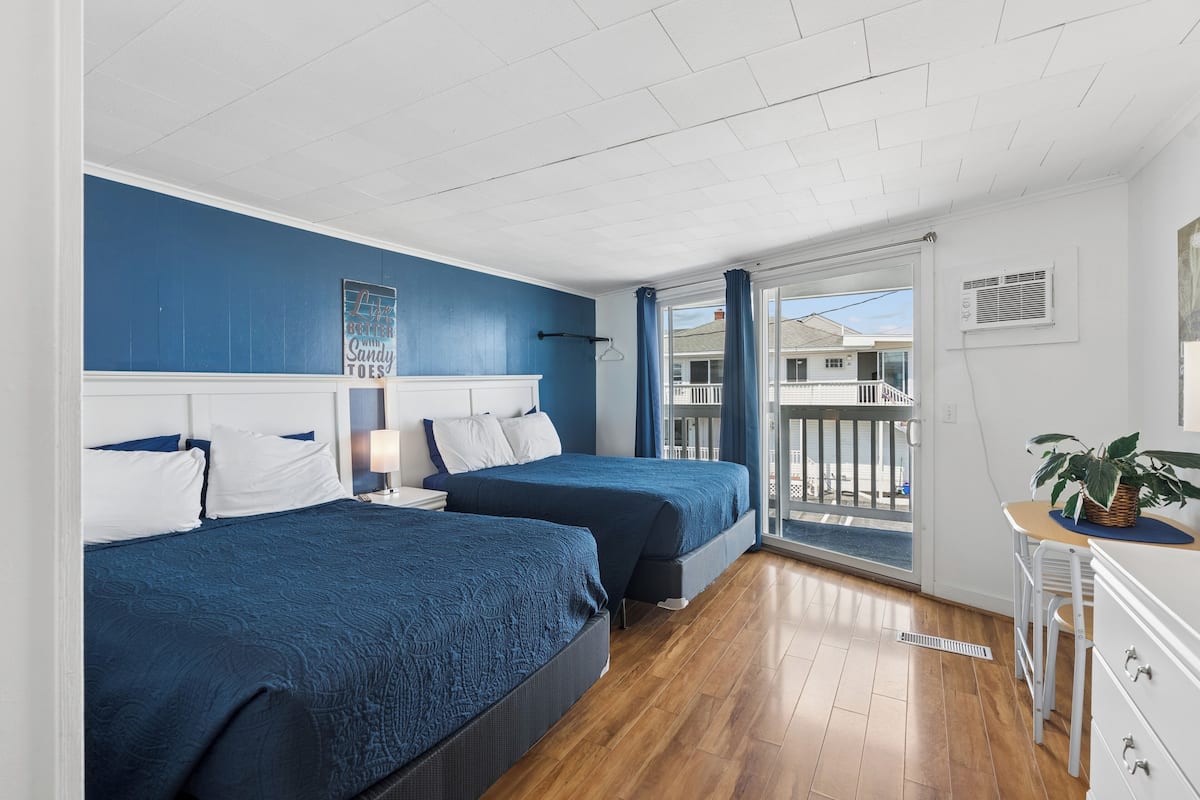 A hotel room with two beds, a balcony with a view, a small table with a plant, and a window with curtains.