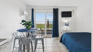 A room with a bed, a TV, a table with chairs, a potted plant, and a view of the sea. - Atlantis Motel (Old Orchard Beach)