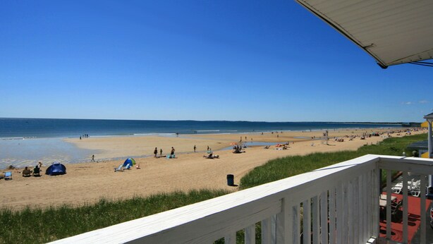 A beach view from a balcony with a railing, a clear sky, and a sandy beach with people and tents. - Atlantis Motel (Old Orchard Beach)