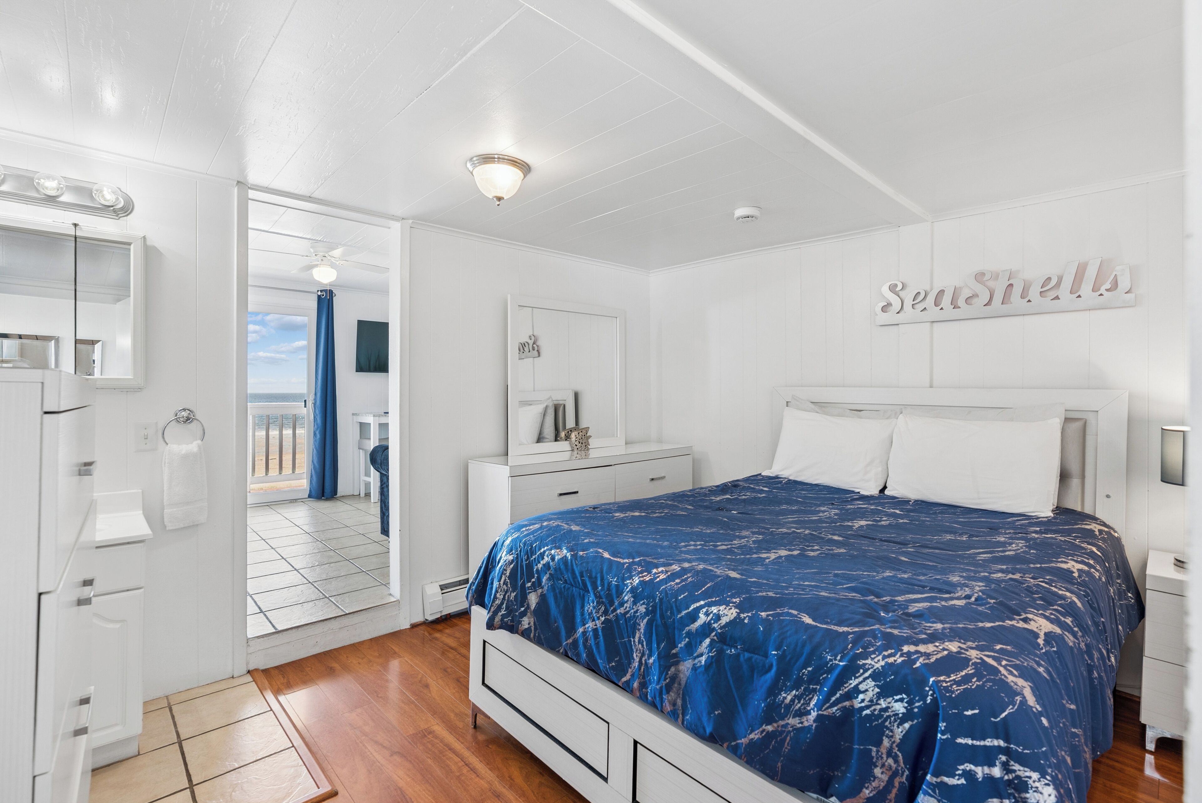 A bedroom with a bed, a nightstand, a dresser, a mirror, and a sign that reads 'Seashells.'