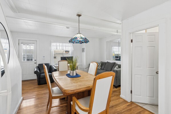 A dining area with a wooden table, chairs, a hanging light fixture, and a sofa in the background. - Atlantis Motel (Old Orchard Beach)