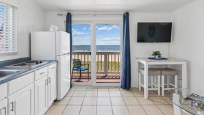 A kitchen with a view of the sea, a dining area with a TV, and a balcony with a chair. - Atlantis Motel (Old Orchard Beach)
