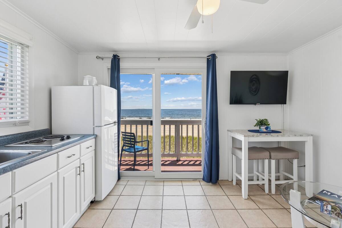 A kitchen with a view of the sea, a dining area with a TV, and a balcony with a chair.