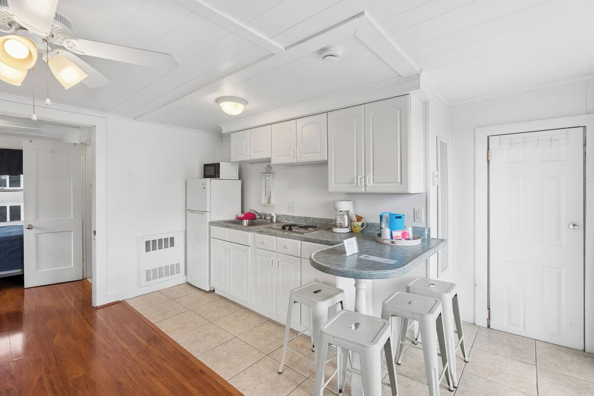 A kitchen with white cabinets, a microwave, a coffee maker, and a small island with stools.