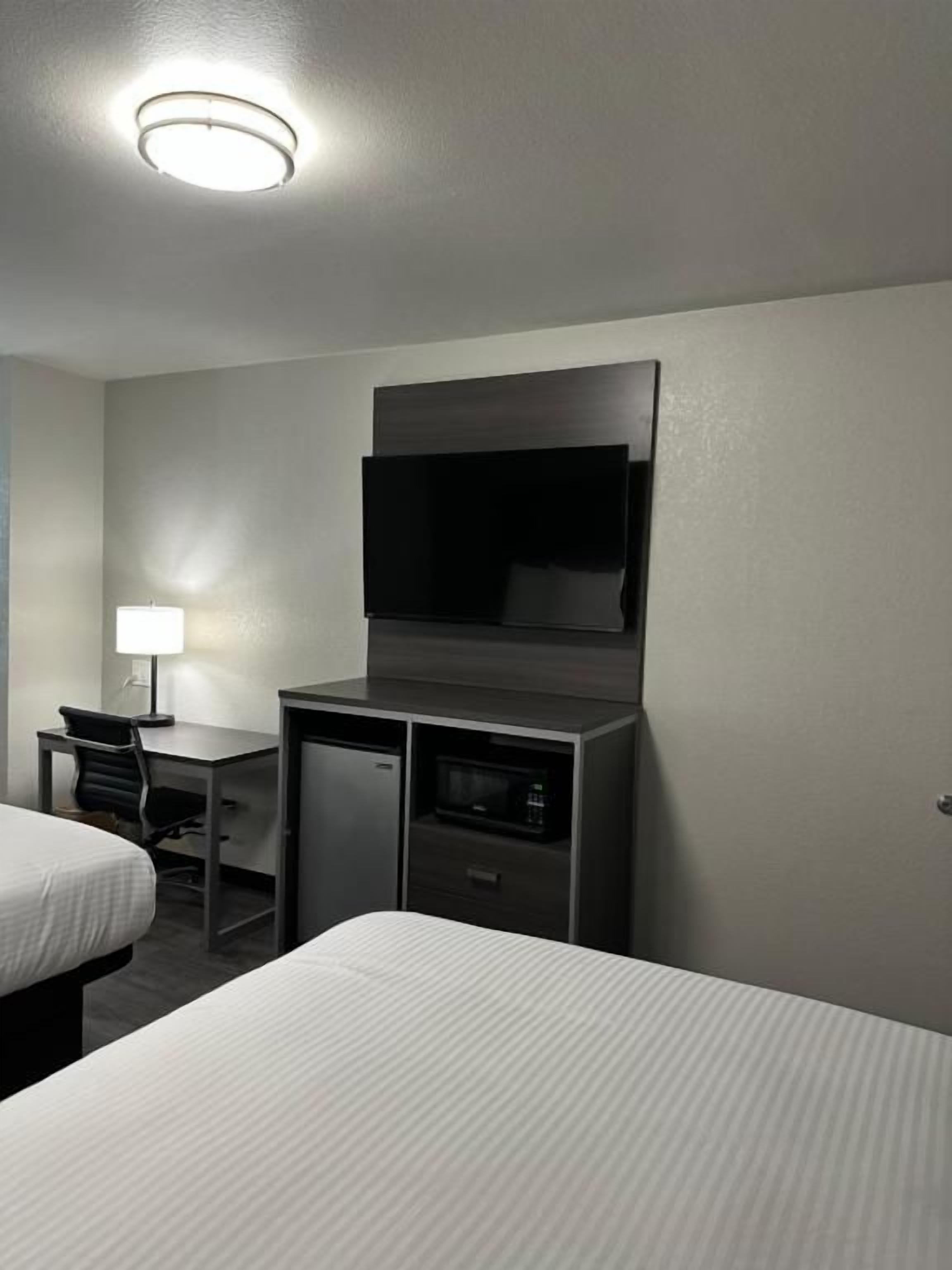 Une chambre d’hôtel avec deux lits, un bureau avec une chaise, un téléviseur fixé au mur et un petit réfrigérateur.