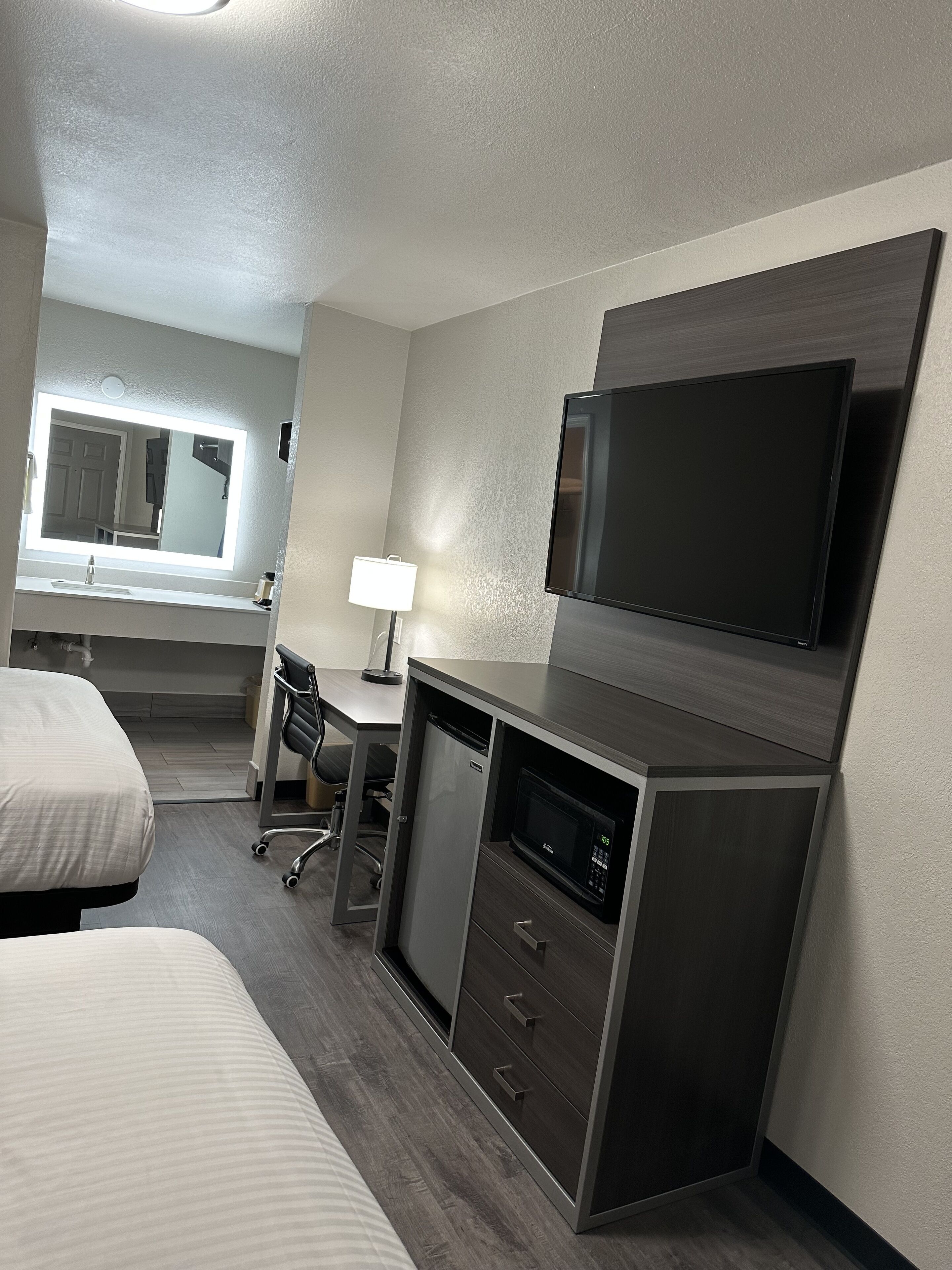 Ein Hotelzimmer mit einem Bett, einem Schreibtisch mit Stuhl, einem Fernseher, einer Mikrowelle und einem kleinen Kühlschrank.