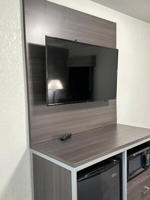 A flat-screen TV mounted on a wall above a kitchen counter with a microwave and dishwasher below.