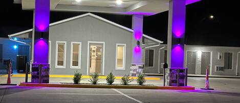 A gas station with a single-story building, a canopy, and purple lighting.