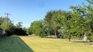 A well-maintained grassy yard with trees and a building in the background. - Sleepy Traveler Motel (Wagoner)