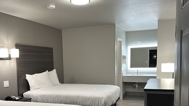 A hotel room with two beds, a desk, a mirror, and a bathroom visible through an open door. - Sleepy Traveler Motel (Wagoner)
