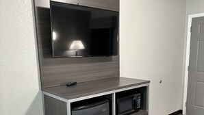 A compact kitchenette with a built-in microwave, a small refrigerator, and a flat-screen TV mounted on a wooden cabinet. - Sleepy Traveler Motel (Wagoner)