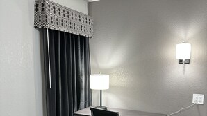 A hotel room with a desk, chair, bedside table, lamp, phone, and air conditioning unit. - Sleepy Traveler Motel (Wagoner)