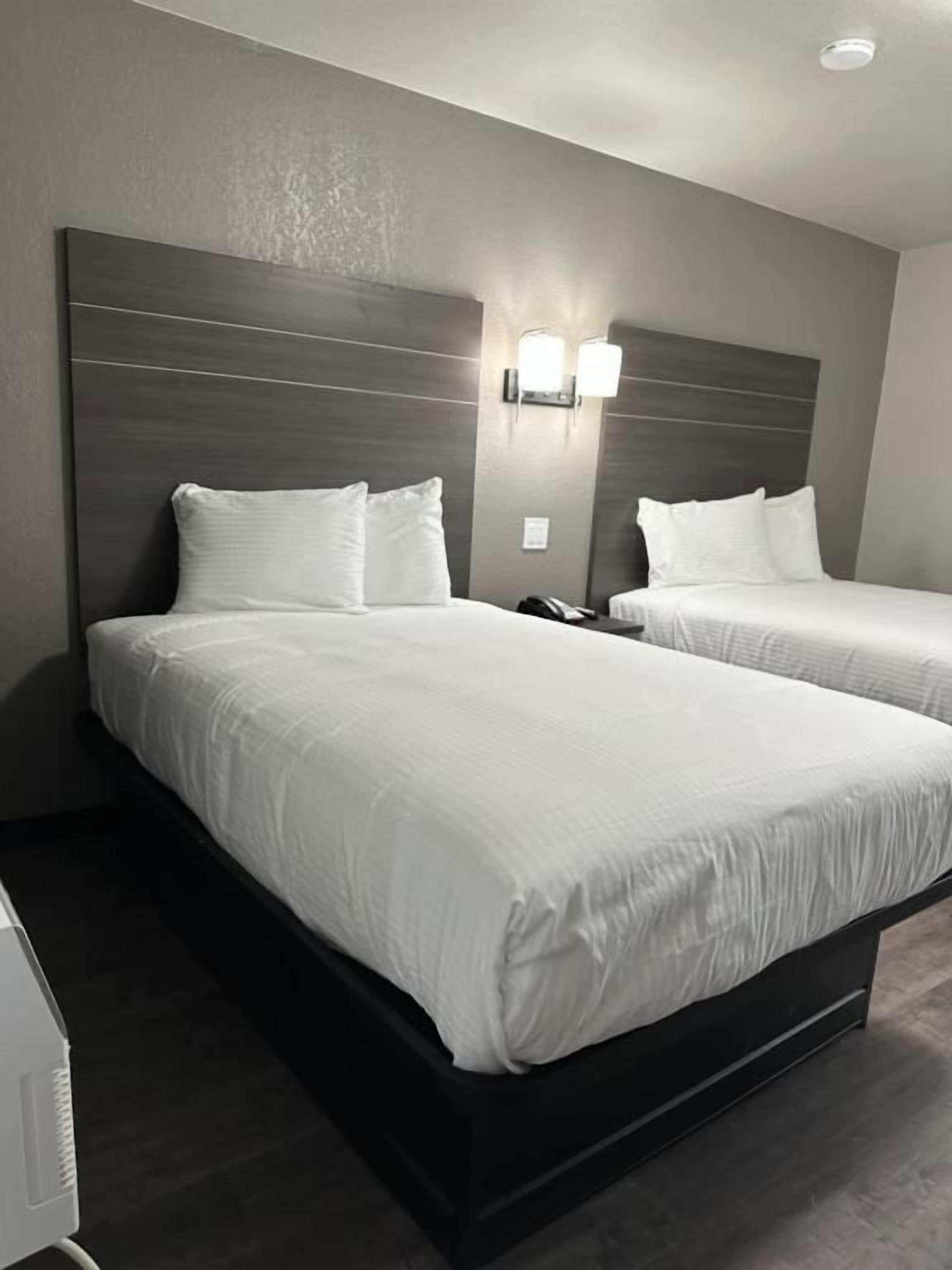 Quarto de hotel com duas camas, cabeceira escura e iluminação na parede.