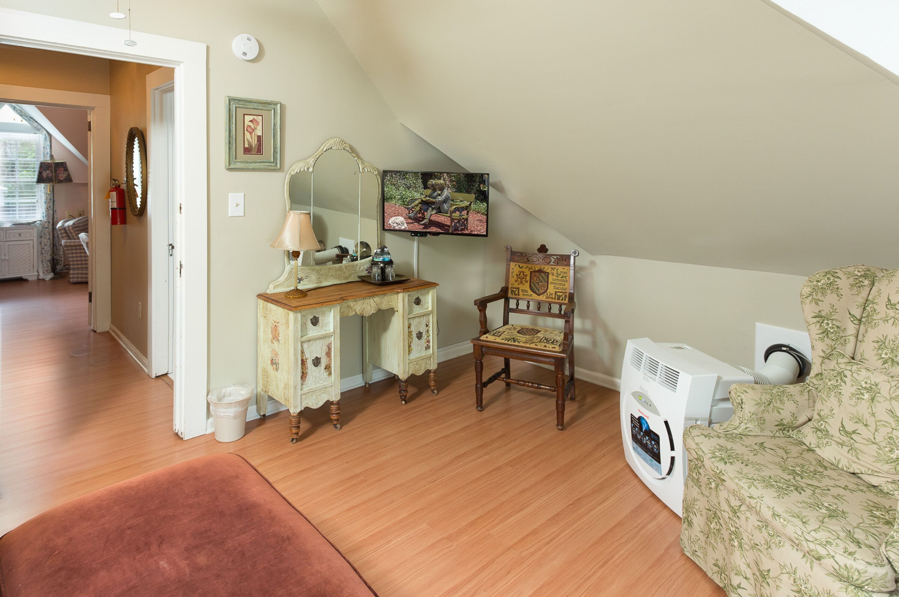 A room with a wooden desk, a chair, a sofa, and a mounted television.