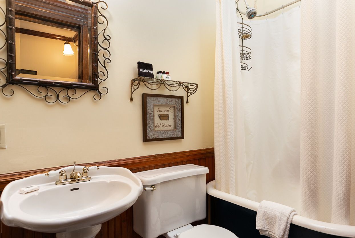 A bathroom with a white sink, a toilet, and a bathtub with a white towel. There is a framed picture on the wall and a shelf with toiletries.