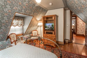 A bedroom with a bed, a wooden cabinet with a television, a chair, and a patterned carpet. - Cedar Crest Inn (Asheville)