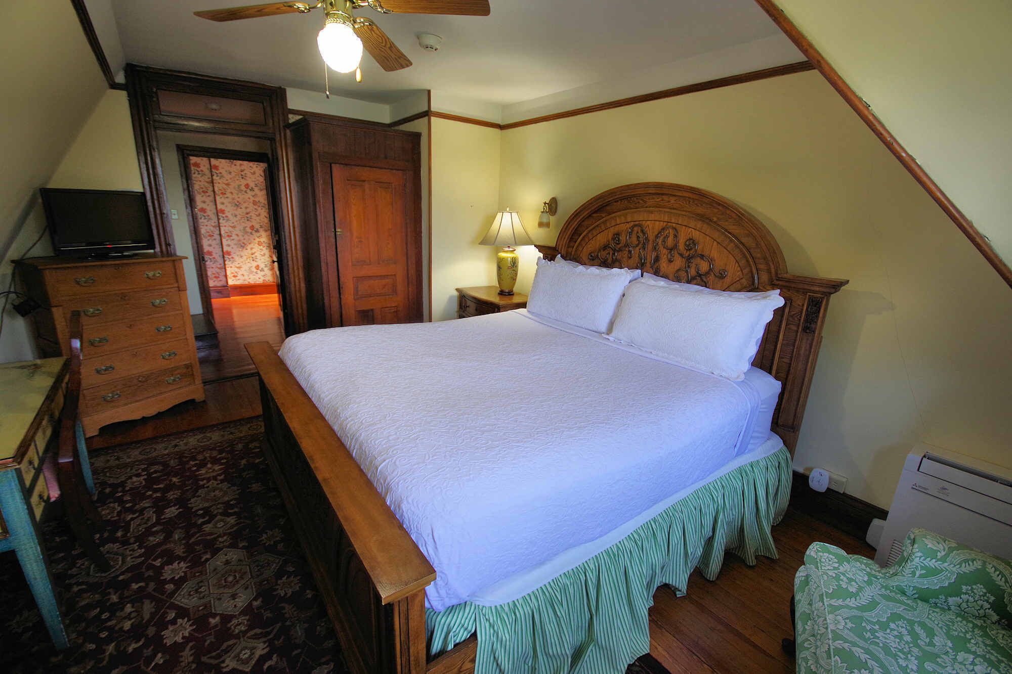 A bedroom with a wooden bed, a nightstand with a lamp, a dresser, and a ceiling fan.