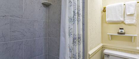 A bathroom with marble tiles, a shower curtain, a toilet, and a shelf with towels.