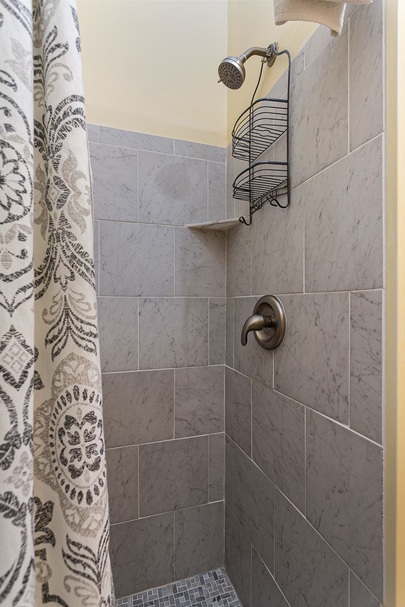 A shower area with grey tiles, a showerhead, and a towel rack.