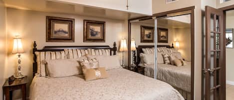 A bedroom with a large bed, two bedside lamps, a ceiling fan, and a mirror on the wall.