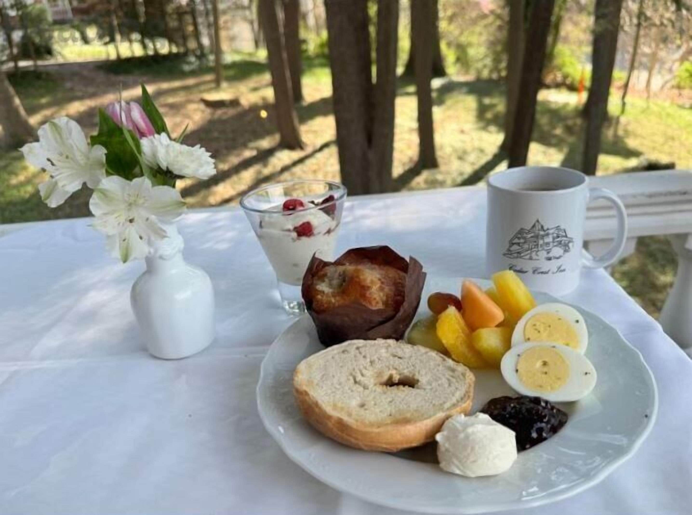 A breakfast setting with a plate of food, a glass of yogurt with berries, a muffin, and a mug on a table outdoors.