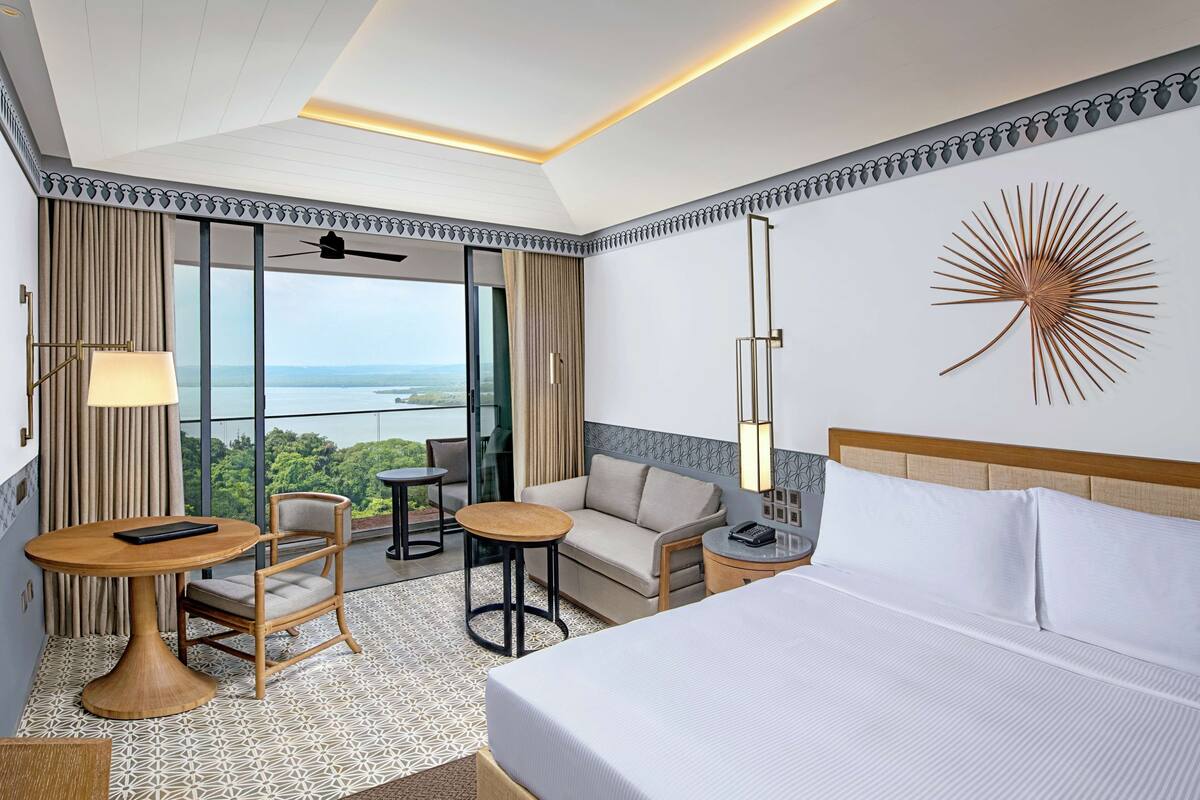 Habitación de hotel con una cama grande, un sofá, una mesa de comedor y vistas al exterior.