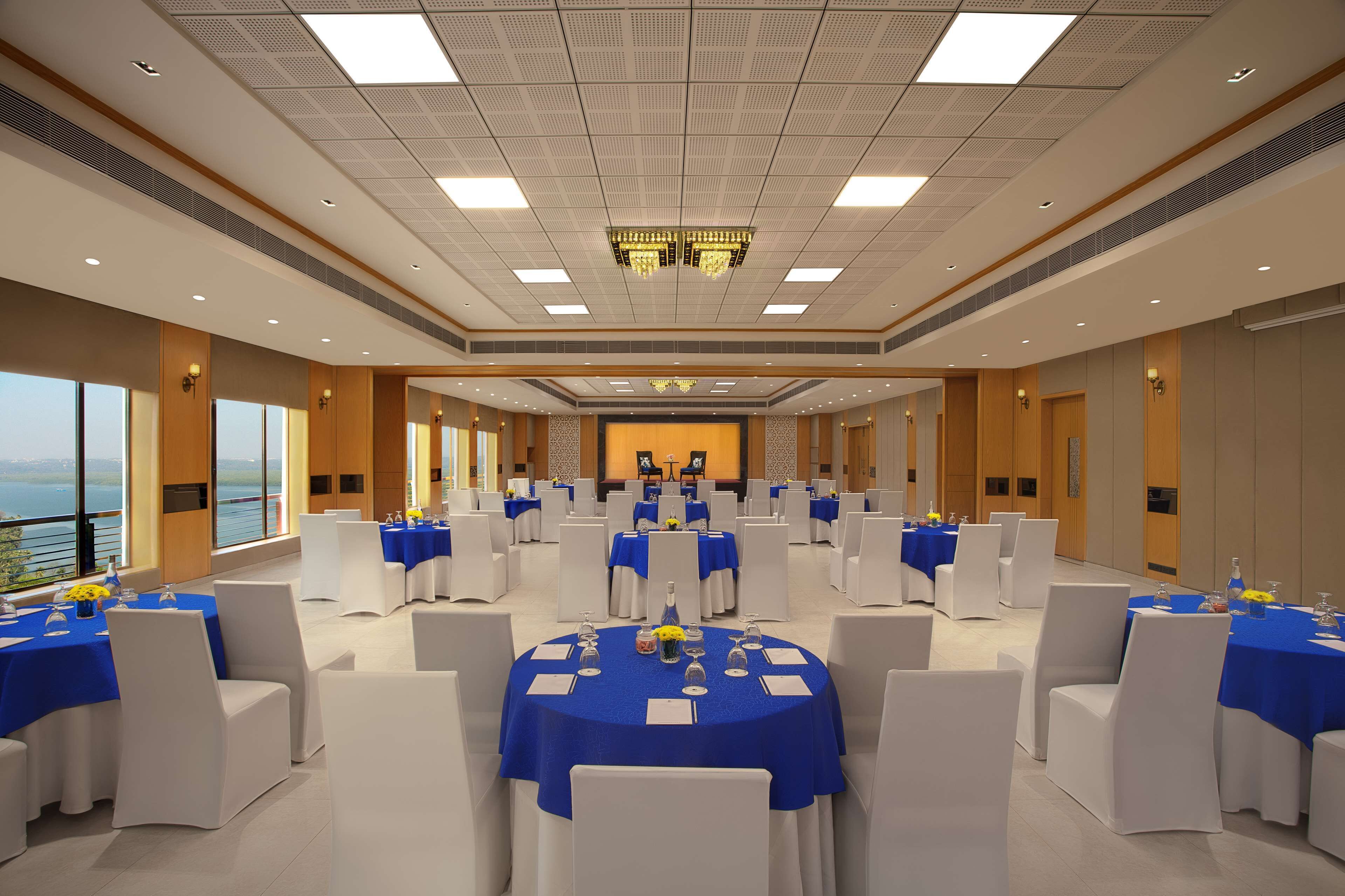 Une salle de conférence avec des tables rondes, des chaises blanches et des nappes bleues.
