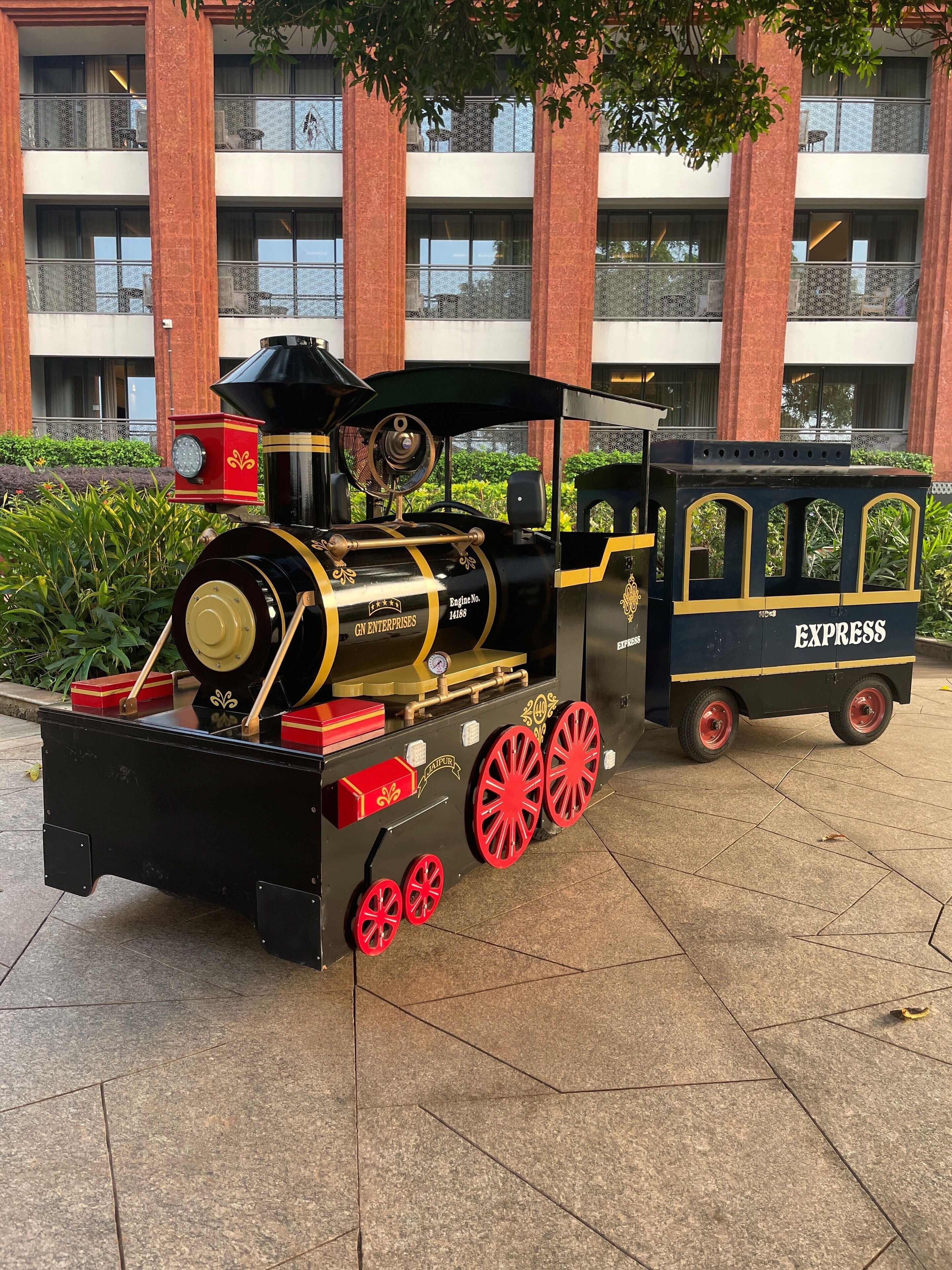 Eine alte Dampflokomotive mit dem Schriftzug "GN ENTERPRISES" und "EXPRESS" an der Seite, geparkt vor einem Gebäude mit roten Backsteinsäulen und Balkonen.