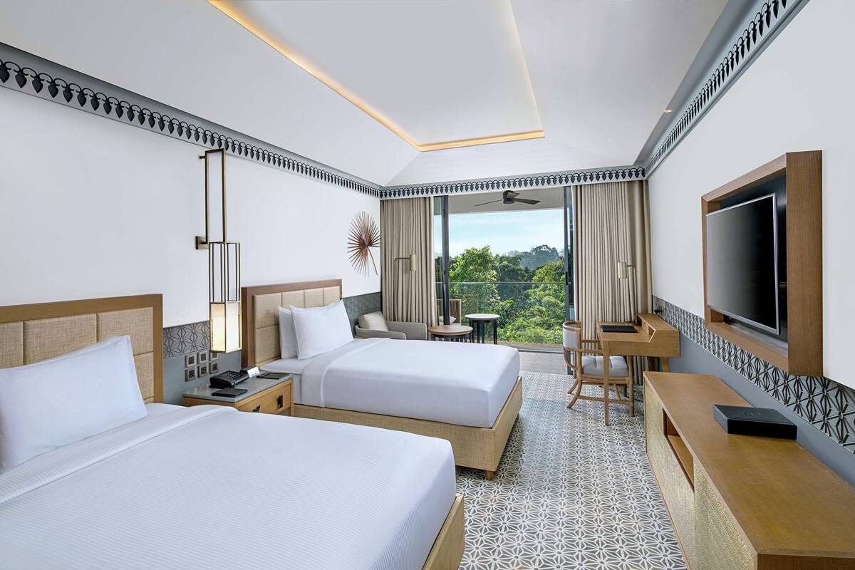 Habitación de hotel con dos camas, televisión, escritorio y balcón con vistas.